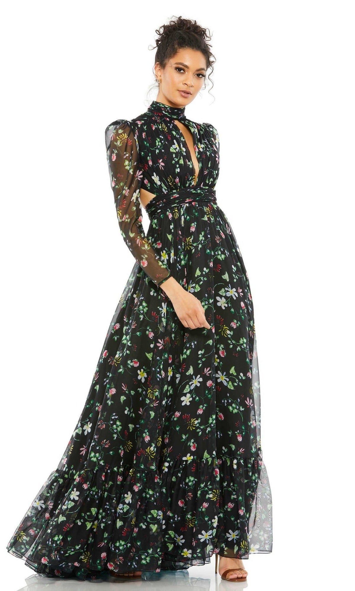A woman models the Mac Duggal 67942 long black print formal dress, featuring sheer long sleeves and a high neckline, set against a white background.